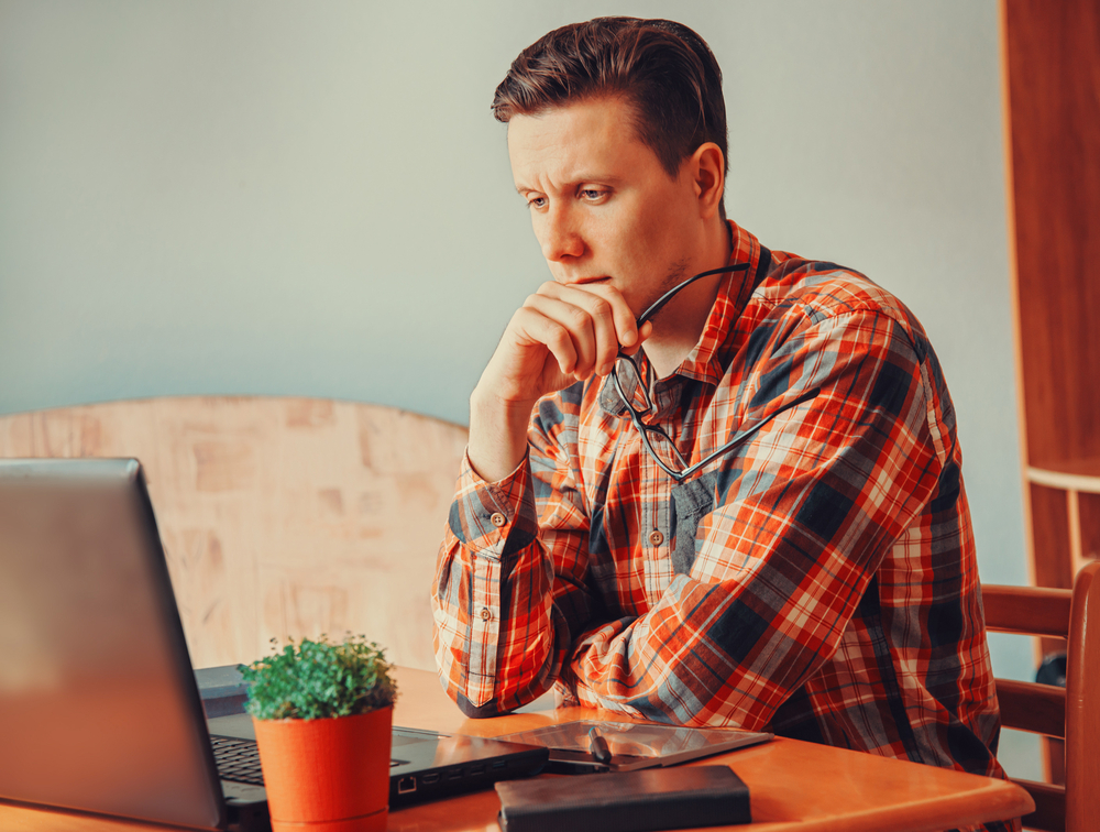 Young man thinking and looking on laptop